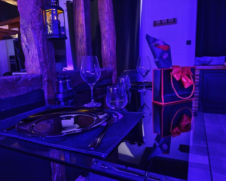 L'espace des gourmands Table en verre dressée avec vaisselle élégante, décoration lumineuse et cadeau emballé.