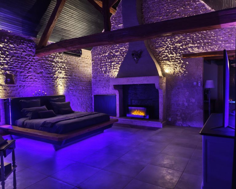 La Chambre - Nid d'amour Chambre XXL moderne avec un lit KING SIZE et un éclairage violet, cheminée décorative. ambiance lumineuse mettant en scène le lieu